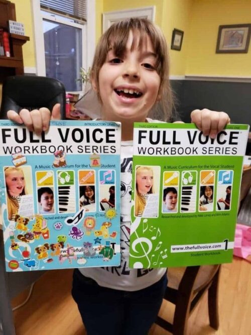 A Child Holding full voice music workbooks and smiling
